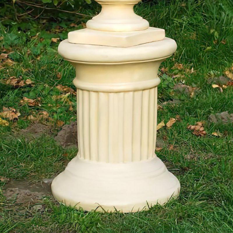 Colonne beige en pierre avec rainures décoratives, posée sur de l'herbe dans un jardin