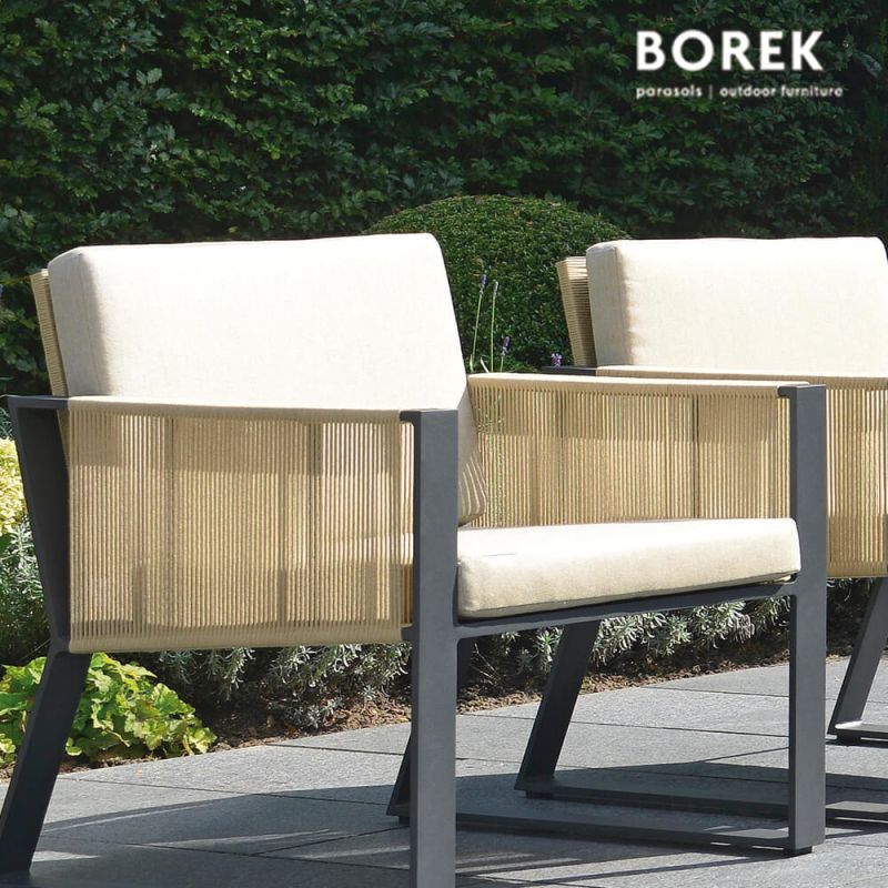 Fauteuil de jardin moderne avec coussin crème et accoudoirs en bois sur une terrasse en pierre dans un jardin