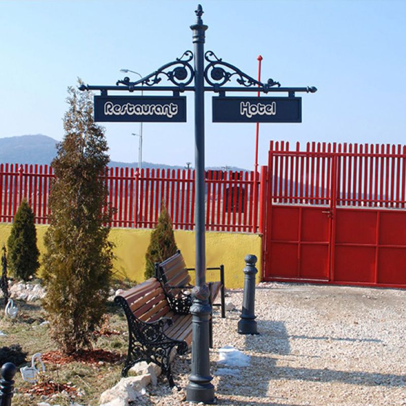 Segnaletica in metallo nero in un giardino con panchine e piante, con cartelli per ristorante e hotel