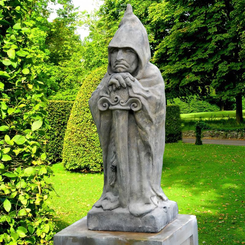 Statue en pierre d'un chevalier à capuche tenant une épée dans un jardin verdoyant
