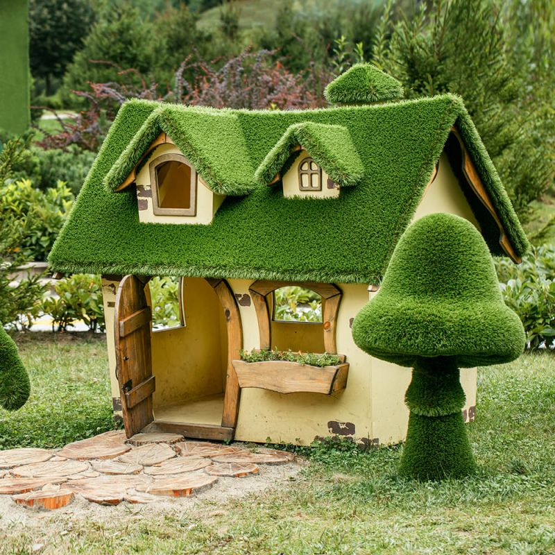 Maison de jardin décorative avec toit en herbe verte et haies taillées dans le jardin
