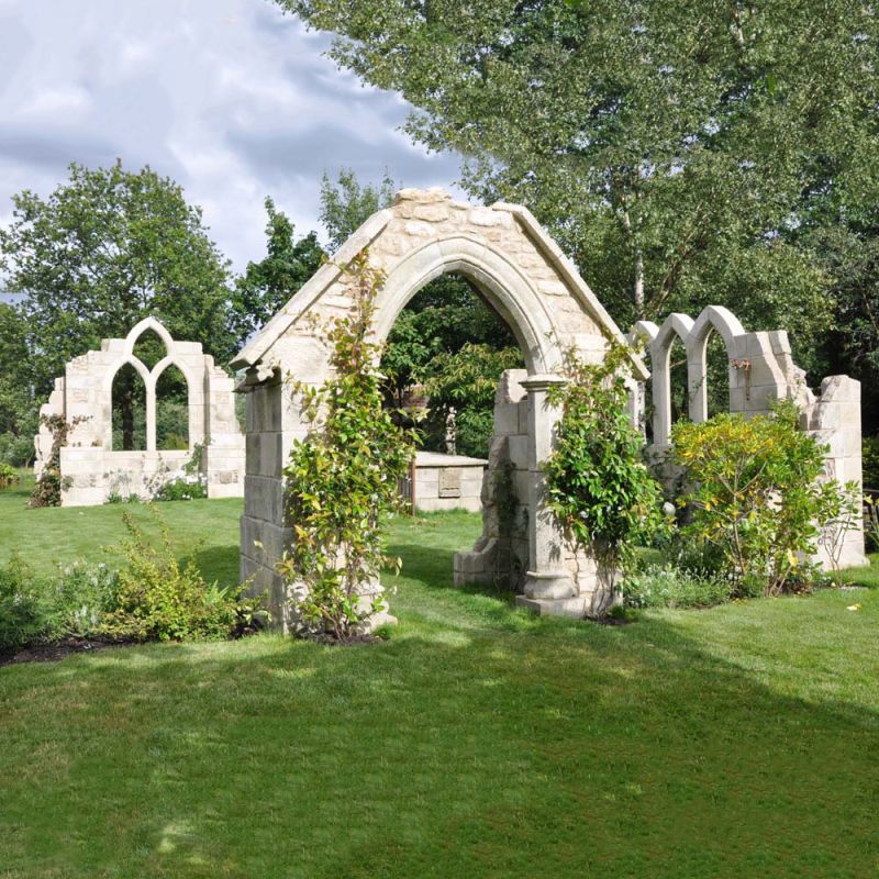 Ruines en pierre avec arcs et plantes grimpantes dans un jardin soigné