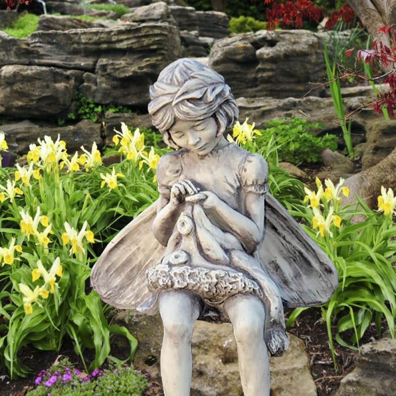 Figura in pietra di una fata seduta tra i fiori nel giardino