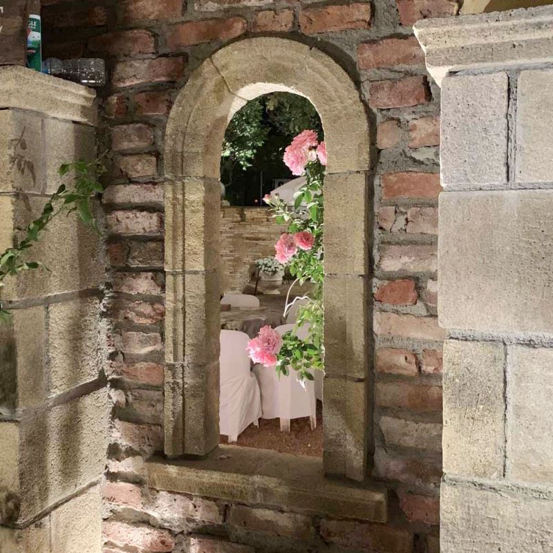 Vista attraverso una finestra ad arco in pietra con rose, decorazione da giardino su un muro di mattoni