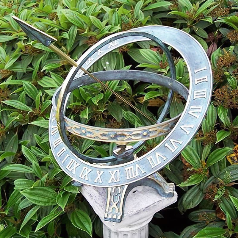 Détail d'une horloge solaire ancienne en métal avec chiffres romains, entourée de feuilles vertes