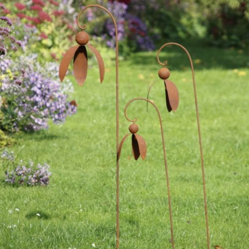 Trois fleurs en métal rouillé sur des tiges courbées dans un jardin sur pelouse verte