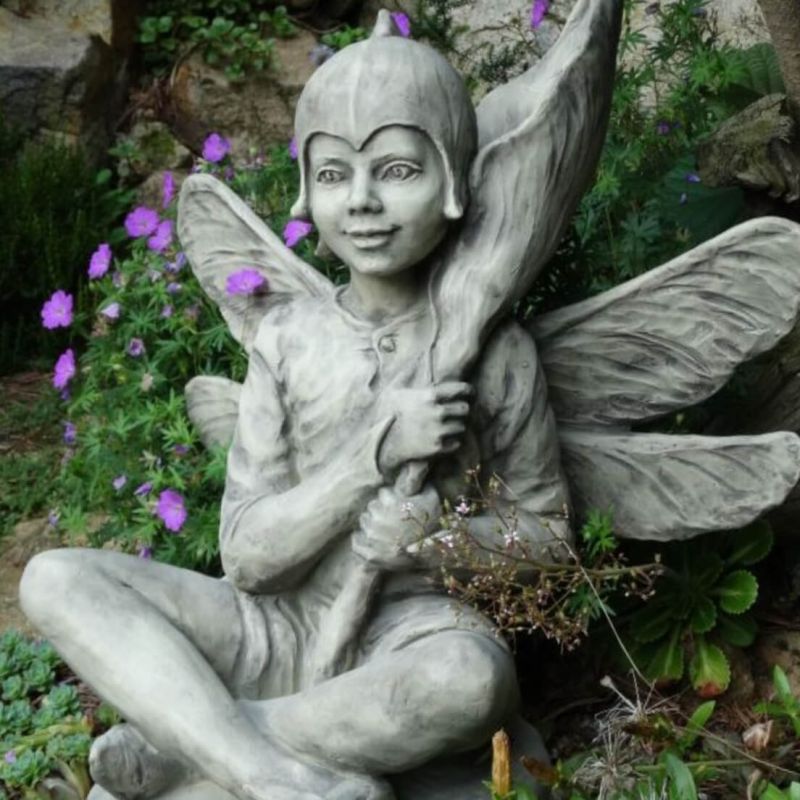 Scultura in pietra di una fata con ali in un giardino con fiori viola