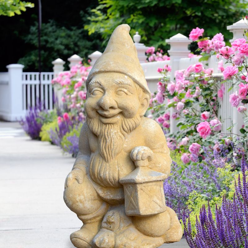 Nain de jardin décoratif en pierre avec une lanterne devant une clôture de jardin fleurie