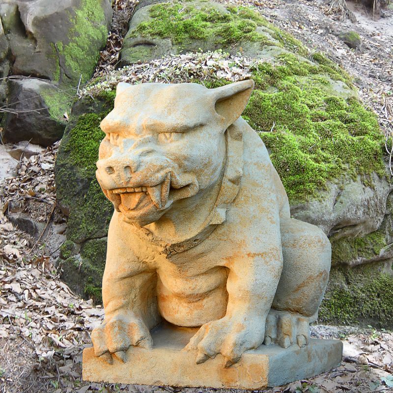 Sculpture en pierre d'un monstre effrayant avec un collier dans une forêt avec de la mousse et des feuilles