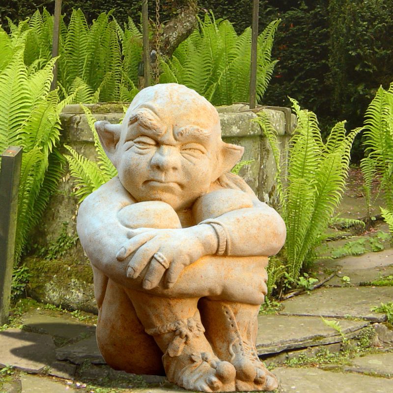 Statue en pierre ressemblant à un elfe dans une pose étrange entourée de fougères dans un jardin