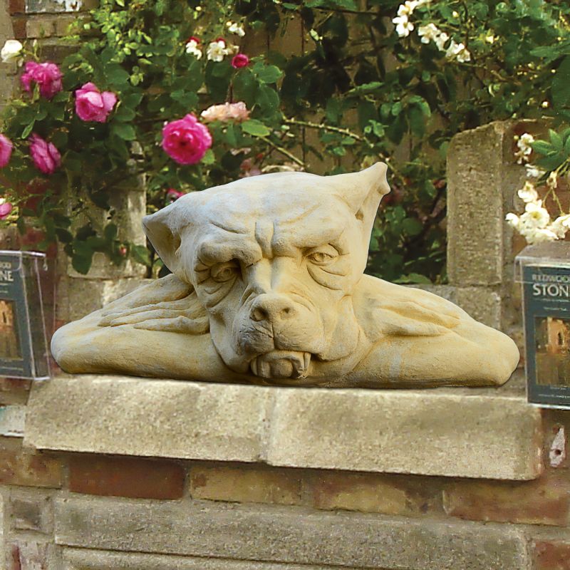 Gros plan d'une statue en pierre représentant un chien couché sur un muret dans un jardin, entouré de roses