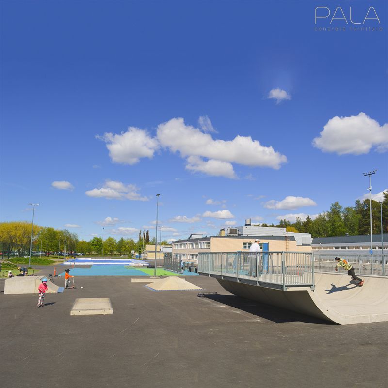 Breiter Skatepark mit Rampen und Skatern bei klarem Himmel und grünen Bäumen im Hintergrund