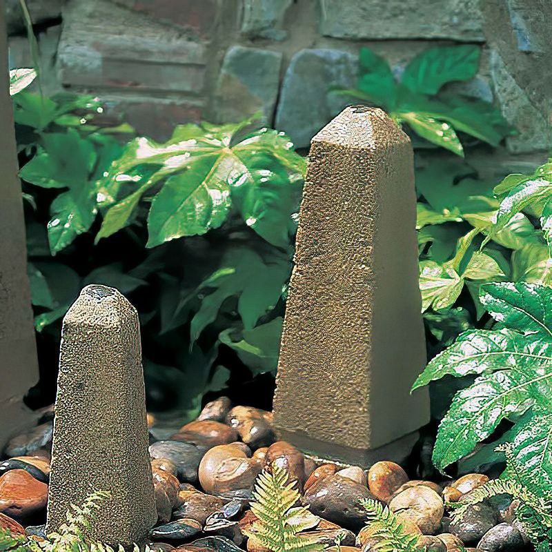 Due stele in granito in un'aiuola di ghiaia con fogliame verde e muro di mattoni sullo sfondo