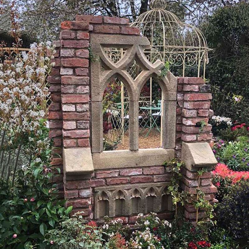 Décoration de jardin en pierre avec fenêtre gothique et cage en laiton dans un jardin fleuri