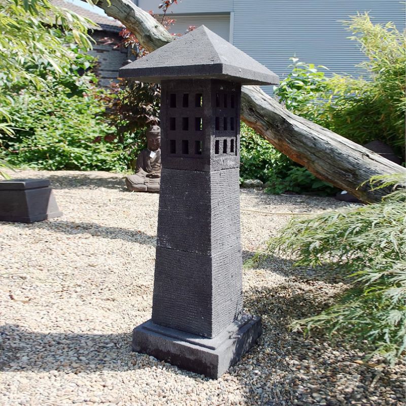 Phare noir en pierre comme décoration de jardin sur un chemin de gravier avec des plantes en arrière-plan