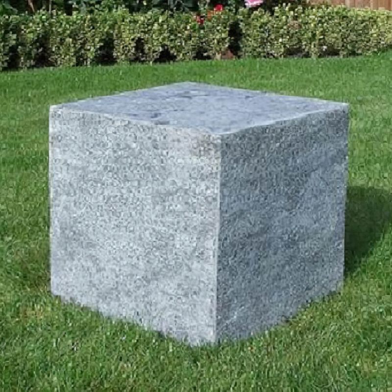 Cube carré en granit gris posé sur une pelouse verte dans un jardin