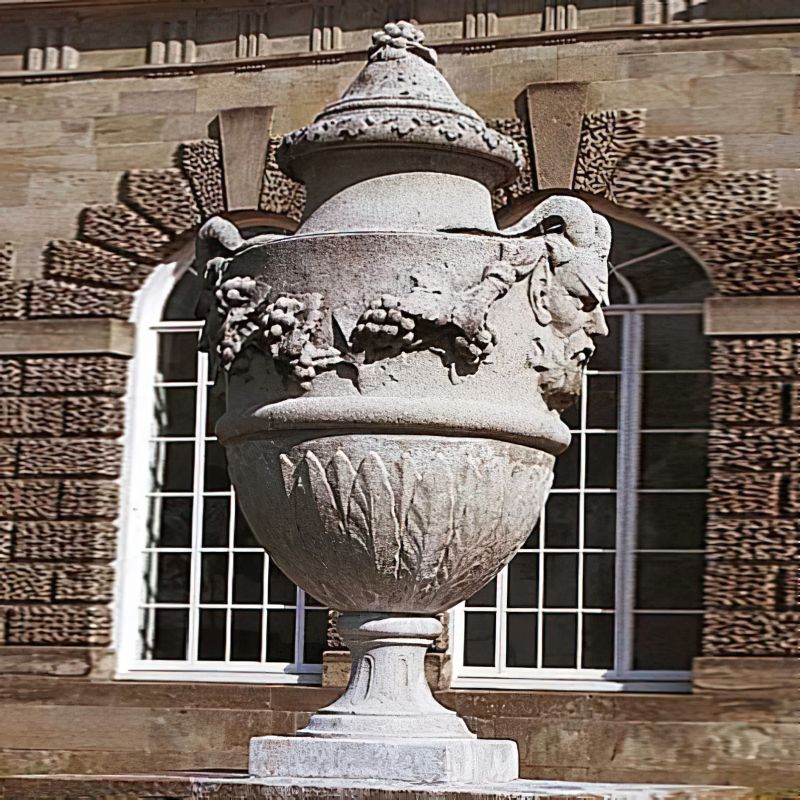 Grande vase décorative en pierre avec des reliefs artistiques devant un bâtiment historique