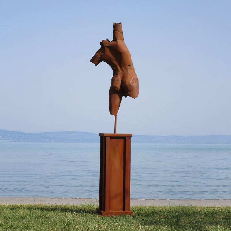 Sculpture en métal rouillé d'une tête de cheval sur un socle au bord d'un lac