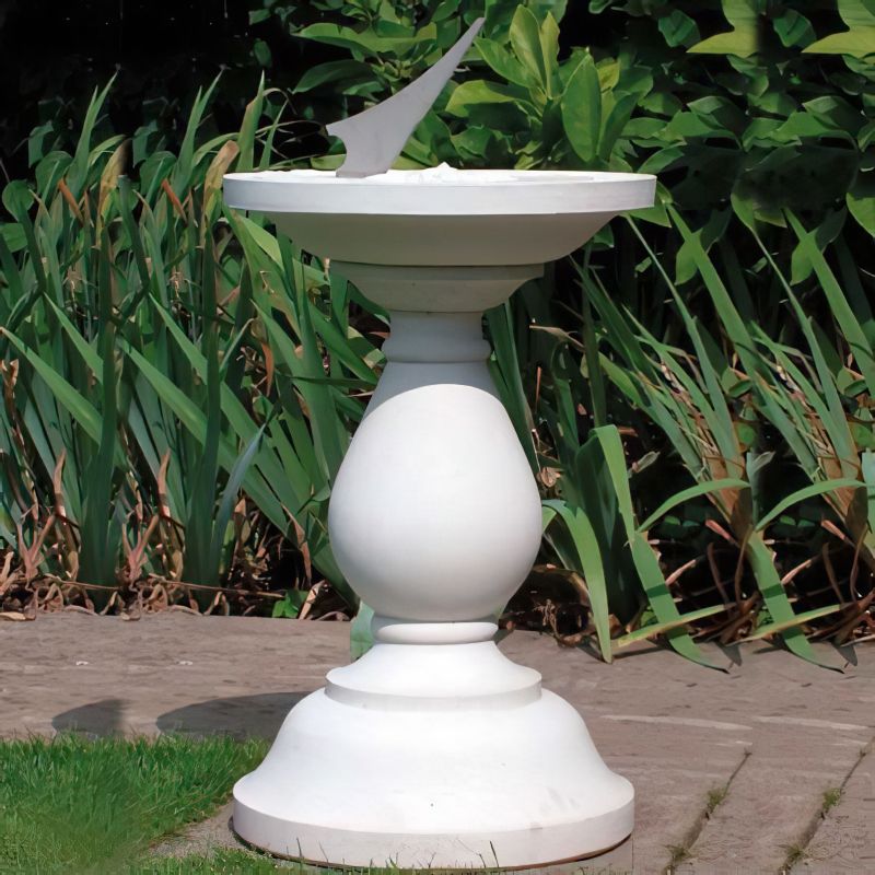 Cadran solaire blanc sur socle dans un jardin entouré de feuillage vert