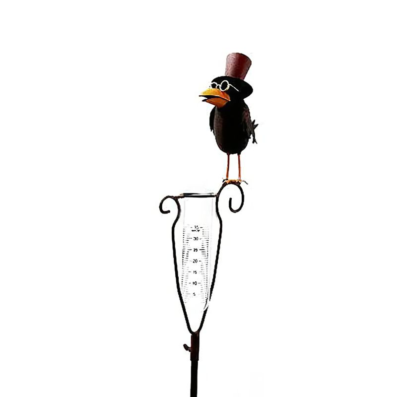 Oiseau en métal noir avec chapeau haut de forme sur un pluviomètre de jardin
