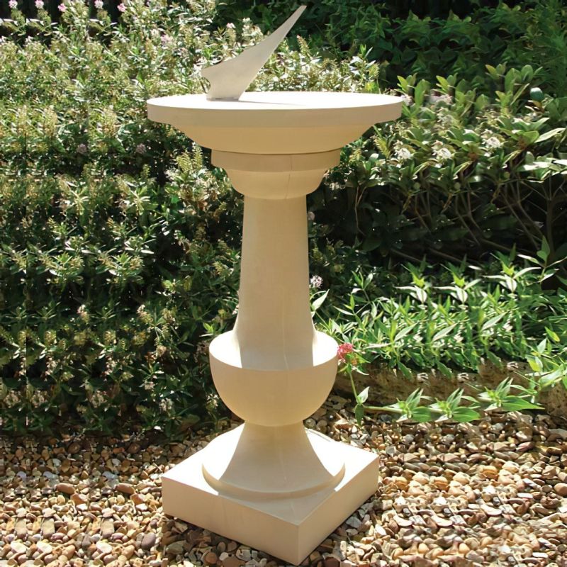 Meridiana in pietra come decorazione da giardino davanti a un cespuglio verde