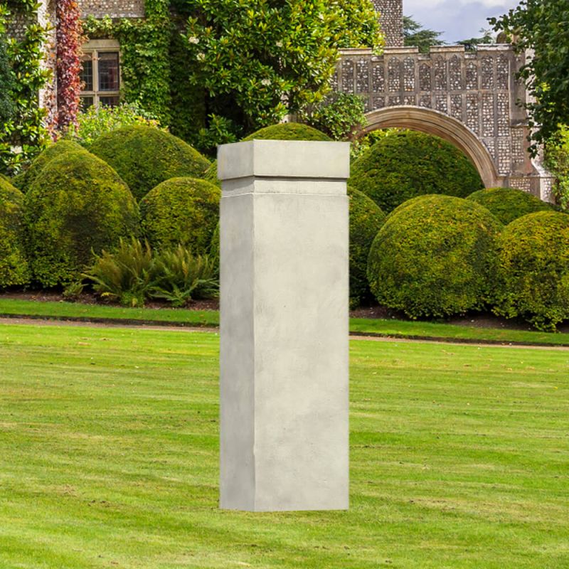 Borne de jardin carrée en béton sur une pelouse bien entretenue devant un jardin avec des haies et une arche