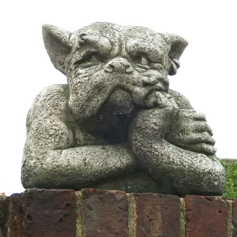 Décoration de jardin en pierre d'un chien d'apparence pensive posé sur un mur