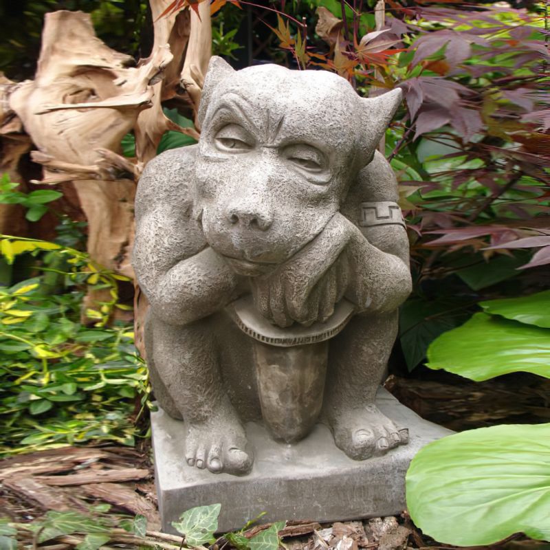 Décoration de jardin : sculpture en pierre d'un gargouille pensif entouré de plantes