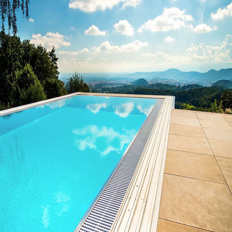 Moderner Pool mit blauem Wasser und Panoramablick auf Berge, umgeben von Steinfliesen und Gartenlandschaft
