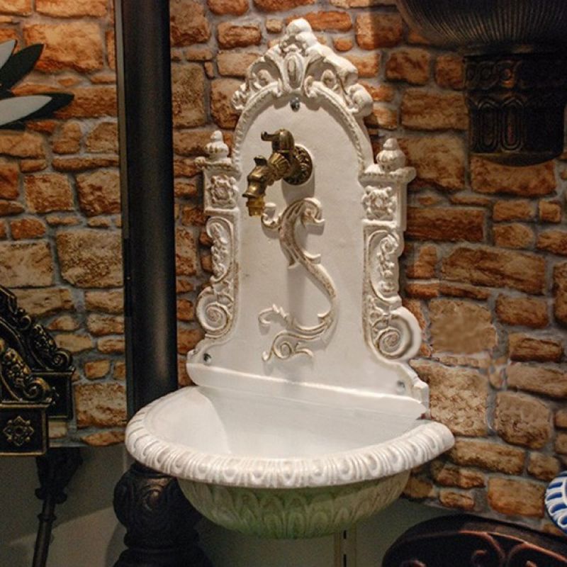 Fontana da parete verniciata di bianco con rubinetto vintage davanti a un muro di pietra rustica