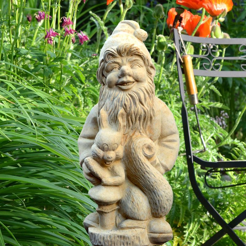 Nain de jardin en pierre tenant un écureuil dans un jardin fleuri à côté d'une chaise de jardin