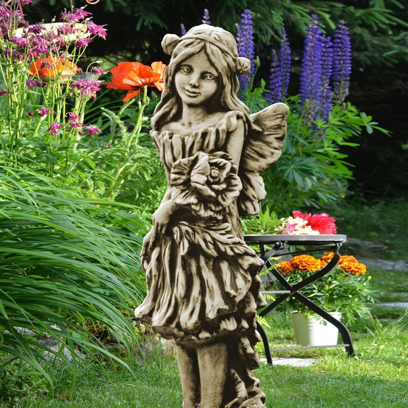 Figura in pietra di una fata come decorazione da giardino tra fiori vari
