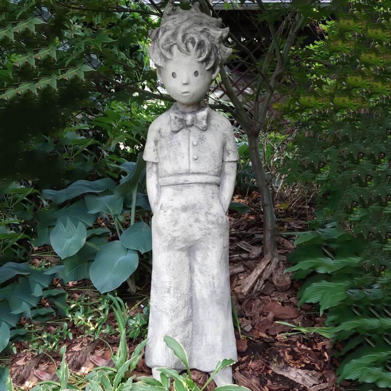 Statua da giardino in pietra raffigurante un ragazzo con bretelle in un giardino verde
