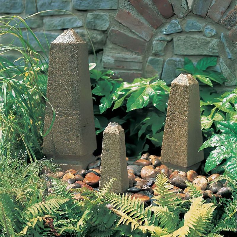 Tre obelischi di pietra di diverse dimensioni posizionati in un giardino con piante e sassi