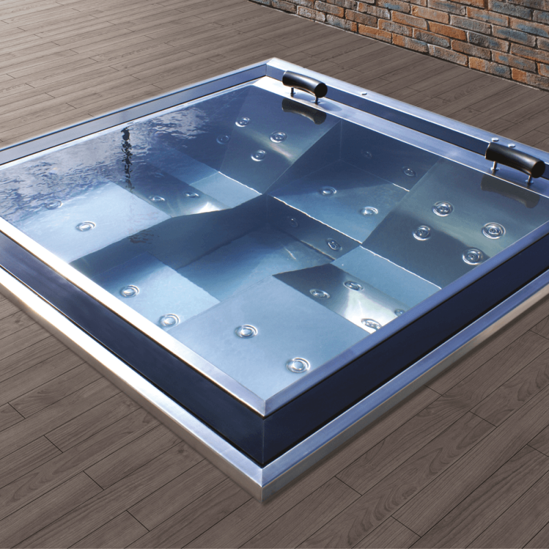 Vasca idromassaggio blu moderna con getti massaggianti su terrazza in legno di fronte a un muro di mattoni