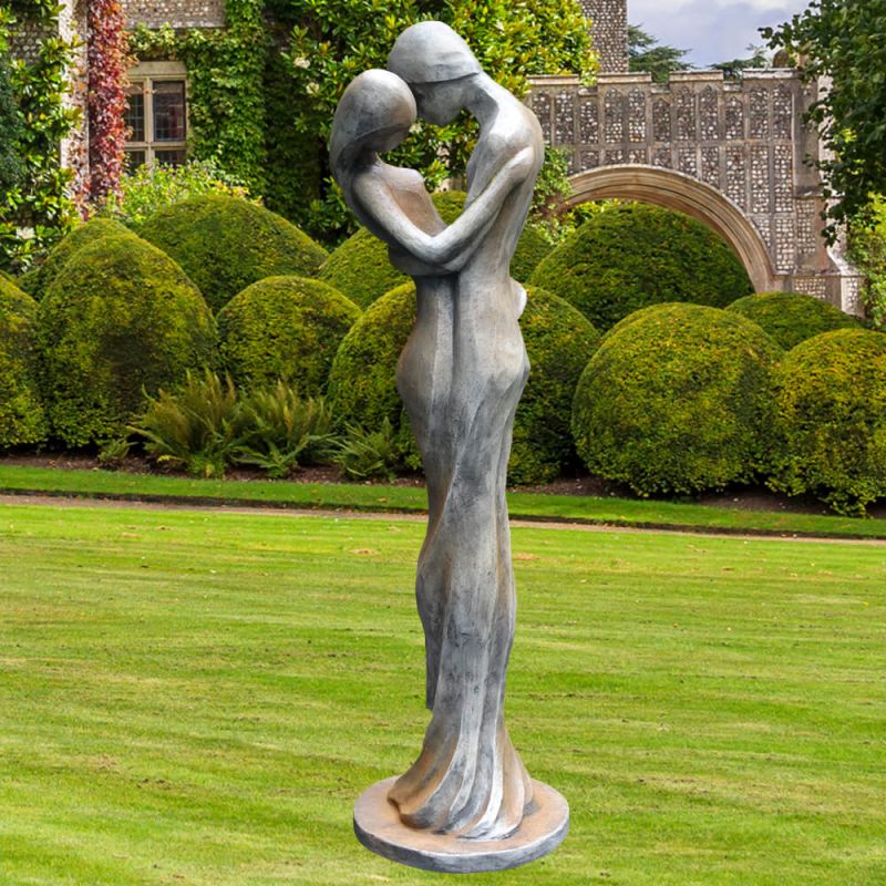Sculpture en métal d'un couple enlacé sur une pelouse verte avec des buis arrondis en arrière-plan