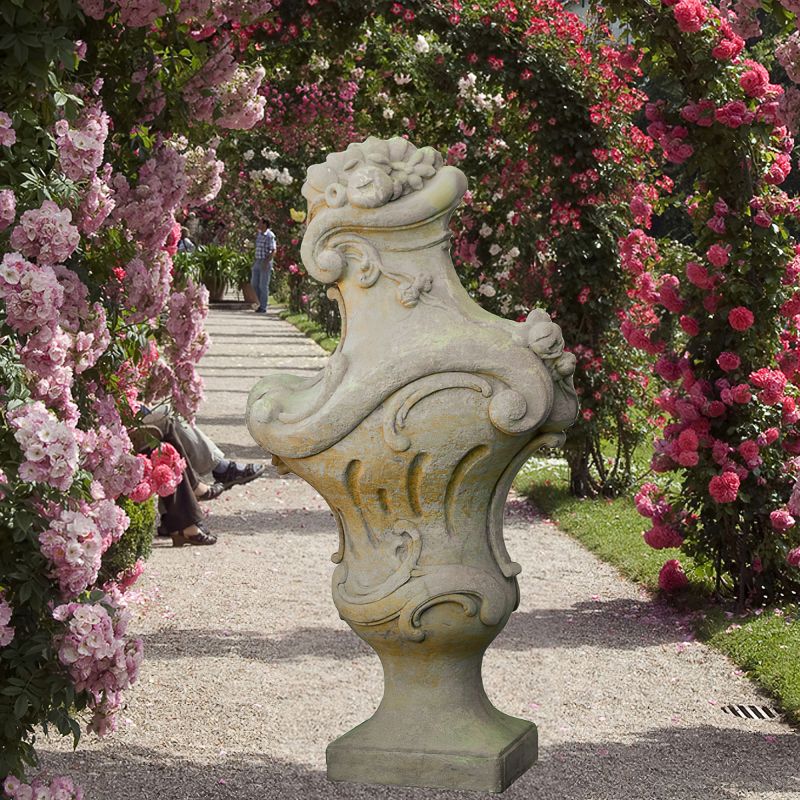 Élégante sculpture en pierre devant une arche de roses dans un jardin soigné