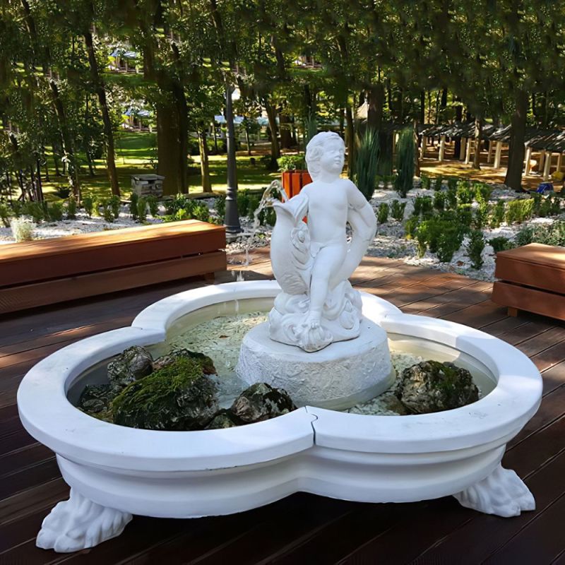 Fontana da giardino bianca con scultura di bambino, circondata da terrazza in legno e alberi