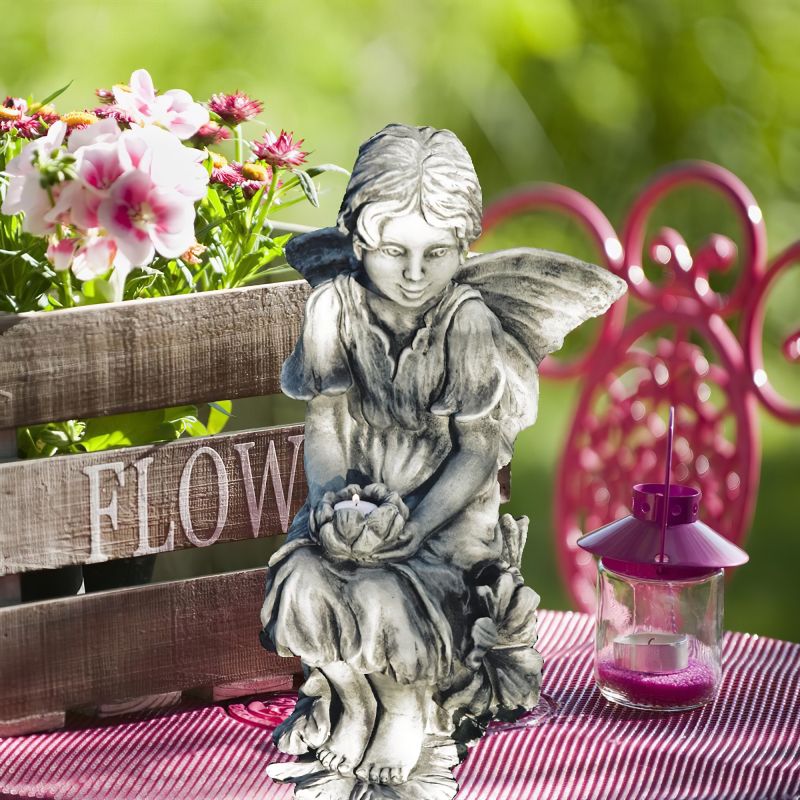 Statua di fata in pietra su tavolo da giardino con cassetta di fiori e lanterna decorativa