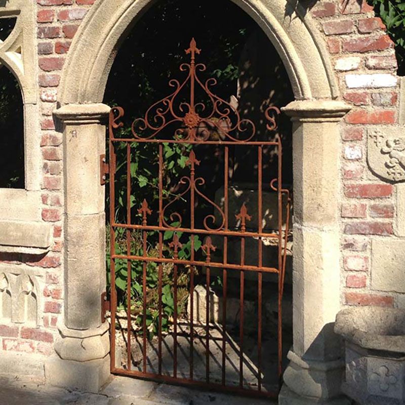 Porte en métal rouillé avec un design artistique dans une arche en pierre dans le jardin