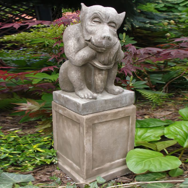 Steinerne Gargoyle-Statue auf einer Steinsäule im Garten mit grünen Pflanzen im Hintergrund