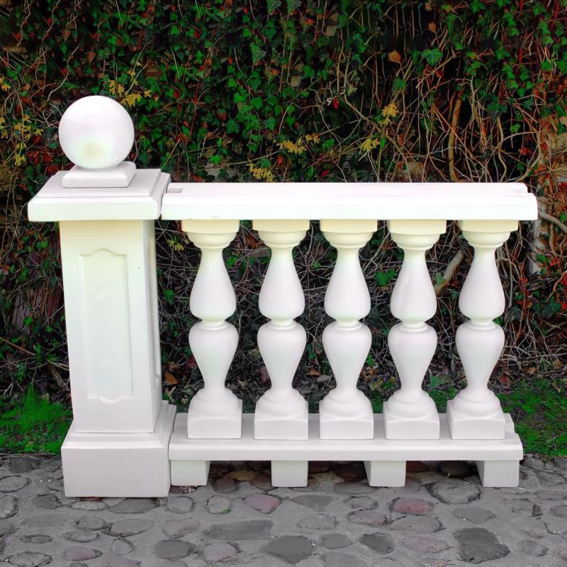 Balustrade blanche en pierre avec décoration sphérique devant une haie