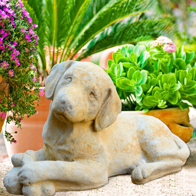 Scultura in pietra di un cane sdraiato in un giardino fiorito con piante