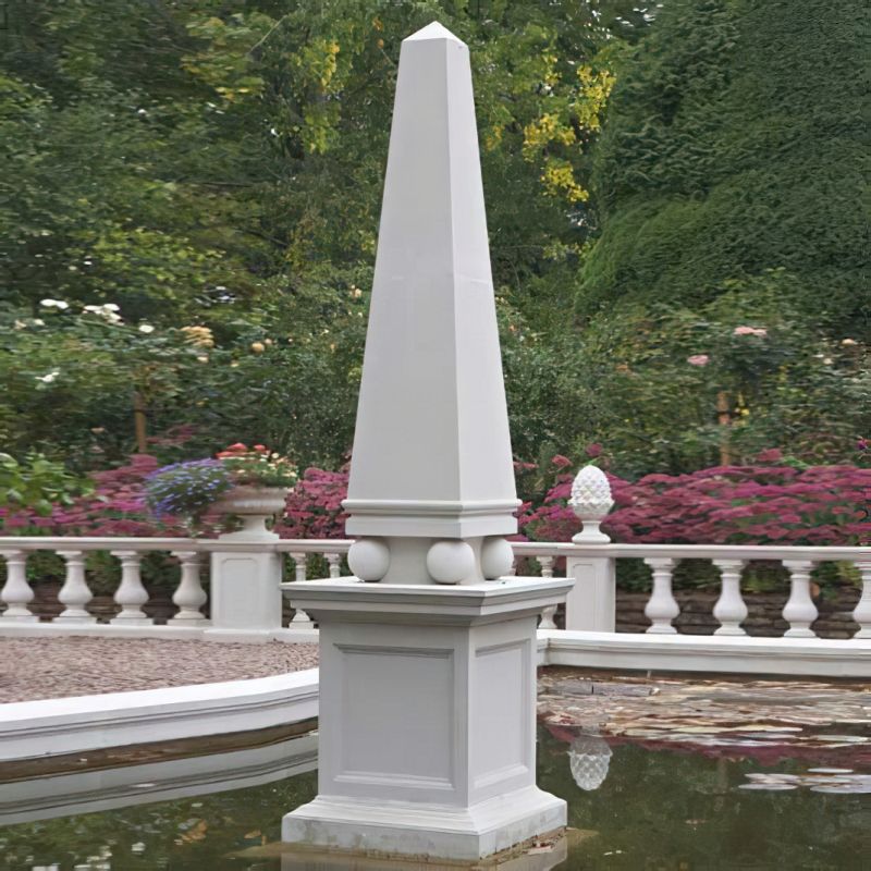 Fontaine d’obélisque blanc dans un jardin soigné avec des fleurs et des arbres