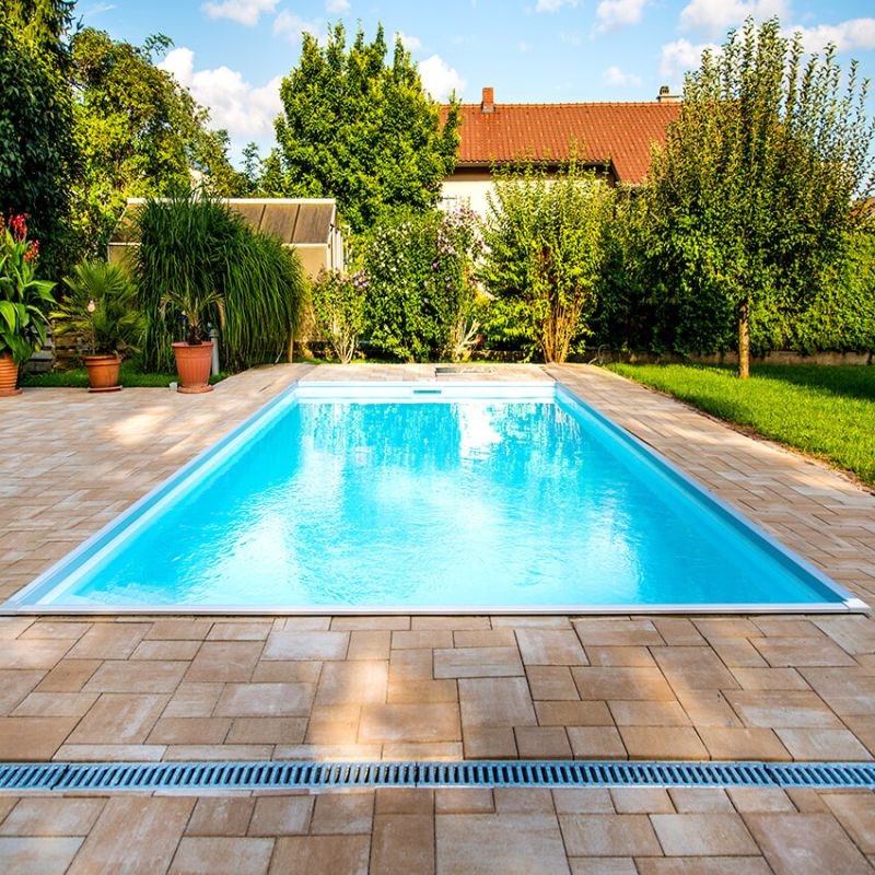 Klare blaue Wasserfläche eines Pools umgeben von Garten mit Bäumen und Terrasse