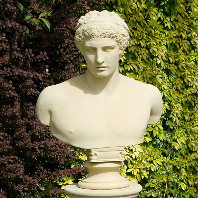 Buste blanche classique d'une figure féminine dans un jardin devant des plantes vertes
