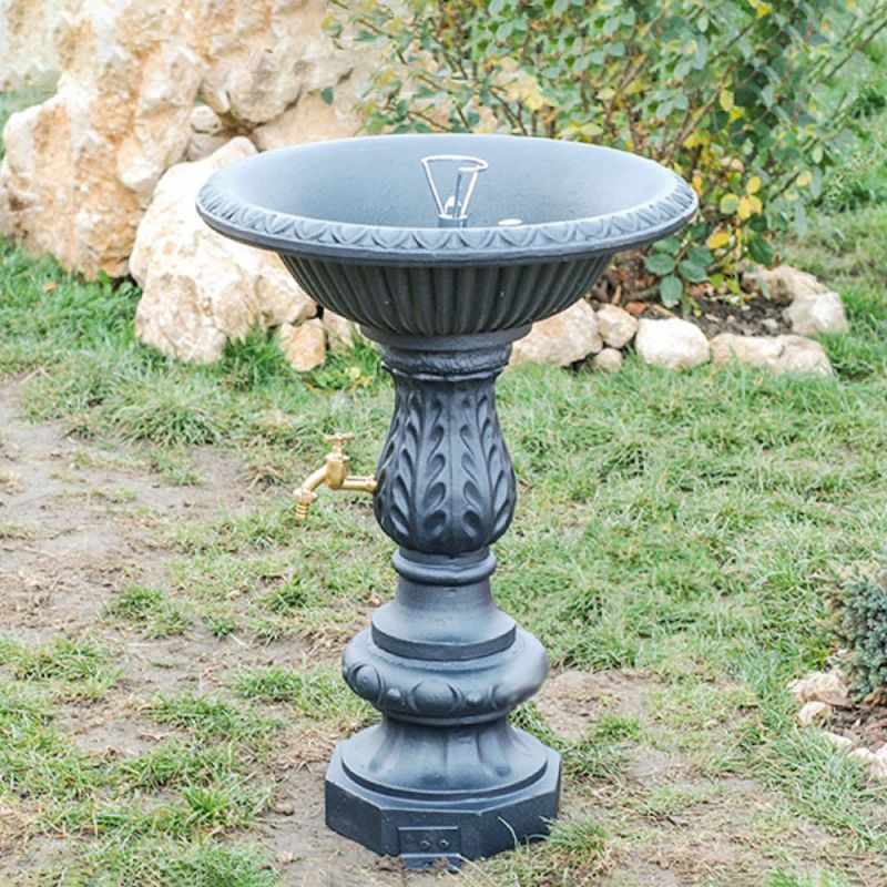 Abbeveratoio nero per uccelli con piedistallo decorato in un giardino davanti a rocce