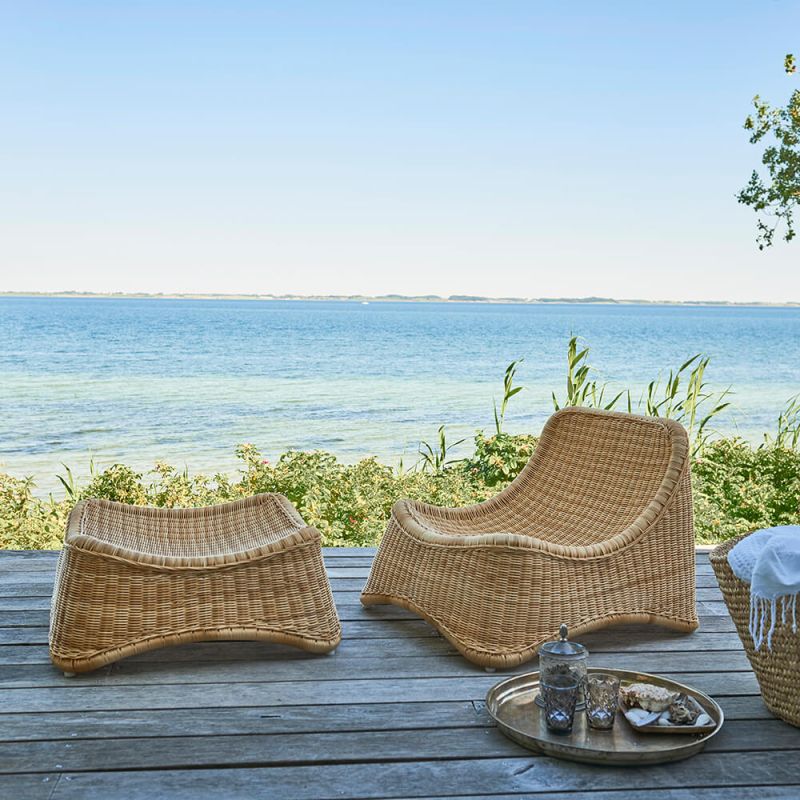 Sedia da giardino in rattan moderna con poggiapiedi abbinato su una terrazza in legno vicino al mare