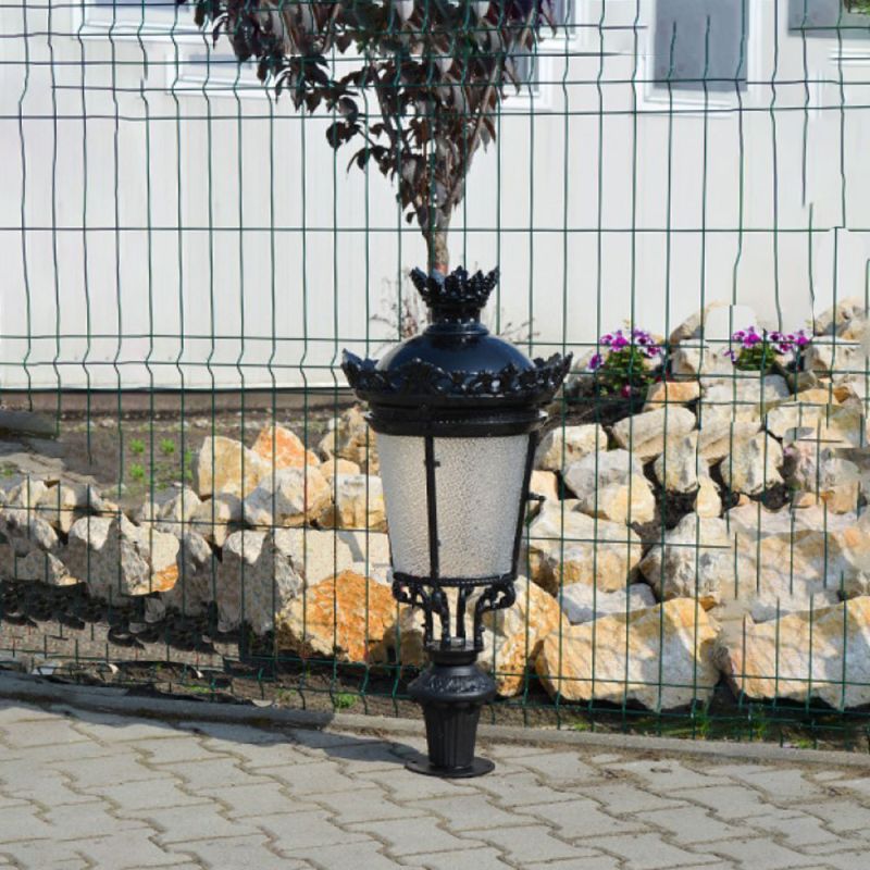 Lanterna da giardino nera con dettaglio a corona davanti a un muro di pietra e a una recinzione