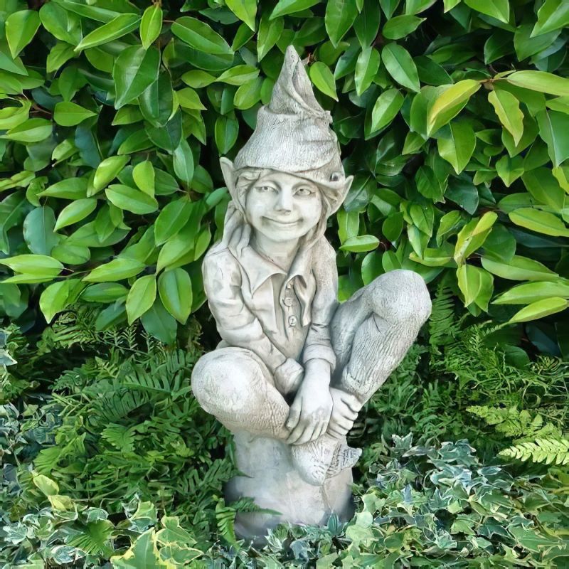 Gnomo da giardino in pietra seduto circondato da piante e foglie verdi